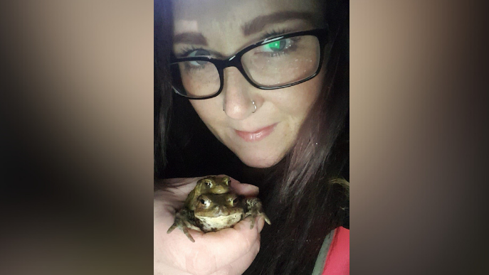 Milly Kennedy holding two toads in her hand while out on patrol. She is looking at the camera.