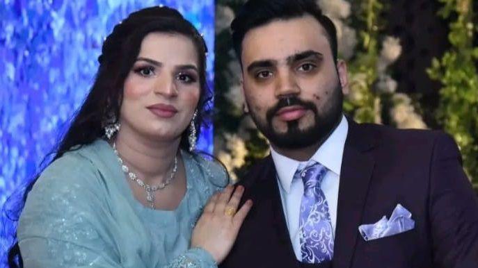 Sharzia Bibi, who is wearing a blue wedding dress, along with an ornate silver necklace and earrings, places her arm against her husband, who is wearing a dark suit with a purple tie and pocket square. 