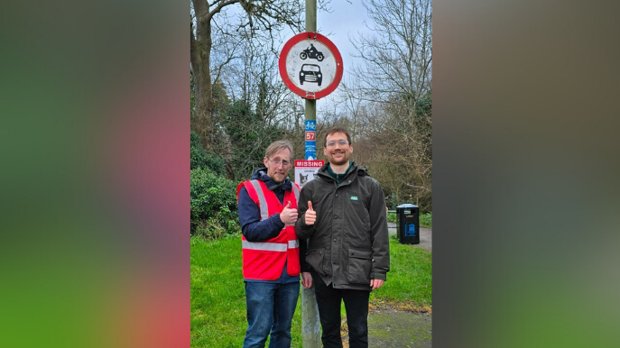 Councillor Charlie Hicks and Labour campaigner Jason Mosley smiling for the camera after cleaning the sign. Mr Mosley is giving thumbs up. It is an overcast day.