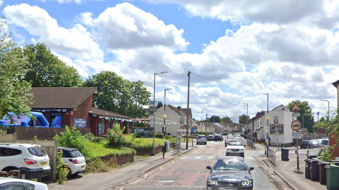 Cars drive up and down part of Gorsebrook Road. There is a pub on one side of the road  with bunting up outside.