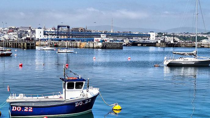 Douglas Harbour on a sunny day, you can see small boats in the foreground, in the background the footbridge at the ferry terminal.