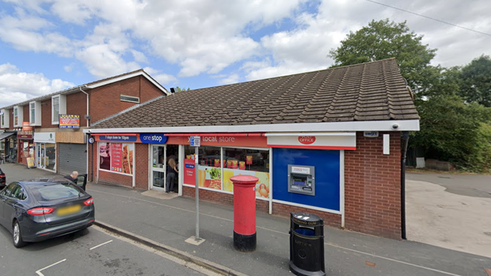 A red brick building that is a post office and "One Stop" convenience store. There is a layby in front of the shop where a grey Ford is parked and a red post box in front of the shop too. 