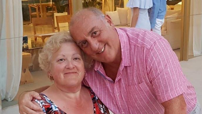 A woman in a floral dress and a man in a pink shirt with his arm around her shoulders