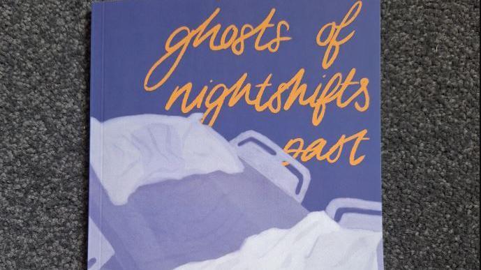 A close up image showing the front cover of Ms Durman's book. It is a dark purple colour with a drawing of an empty hospital bed, which is slightly propped up with dishevelled covers and an indent in the pillow. There is orange scrawled writing across the cover, which reads 'ghosts of nightshifts past'. 