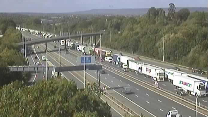The M20 motorway from an aerial vantage point. One side is free-flowing and has few vehicles on it, while there is a long queue of traffic stretching into the distance on the other side.
