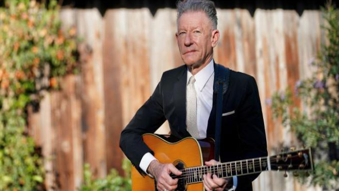 Lyle Lovat in a suit and tie holding a guitar