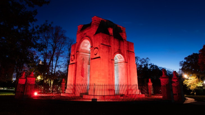 A large war memorial at night, lit up by red floodlights