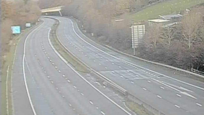 Traffic camera image showing an empty motorway with a bridge in the distance.
