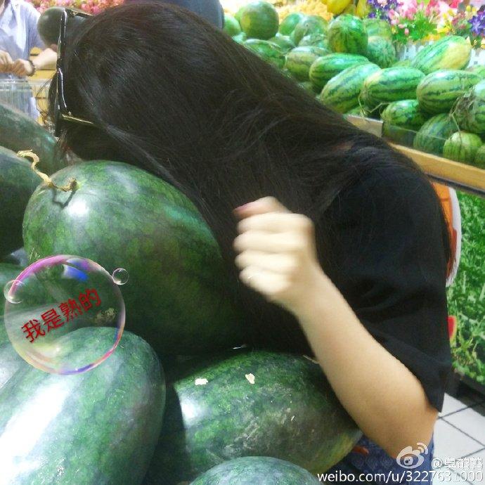 Photo of a woman leaning over a lot of watermelons. Her hair covers her face as she listens to the fruit.