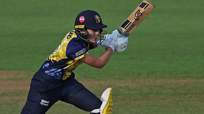 Heather Graham in a dark blue helmet, yellow shirt and dark blue trousers with yellow pads batting for Durham