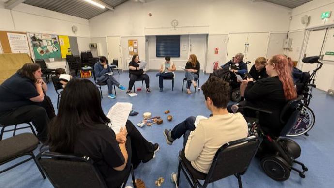People sitting in a circle in a village-hall style room.
