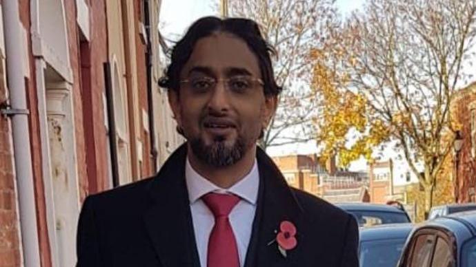 Councillor Salim Desai with overcoat and adorned with a poppy outside the former orphanage