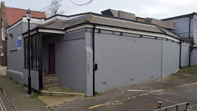 The exterior of the nightclub. It is grey with a black roof and has steps leading to the entrance.