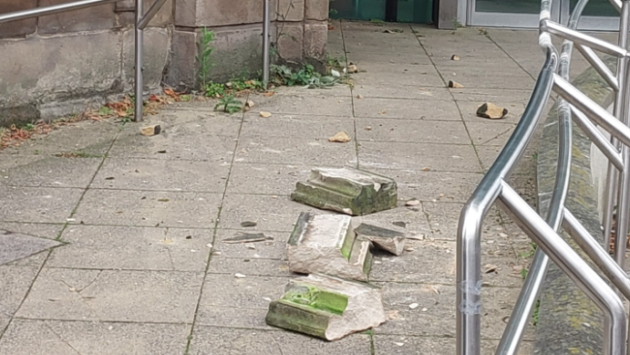 The masonry cracked and broken on a paved section of the area with a metal railing in the front