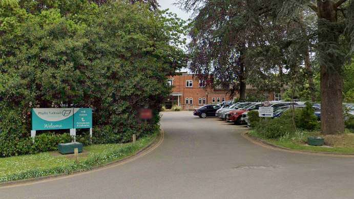 The entrance to a red-bricked building. There is a blue and white sign for the hospice on the left.