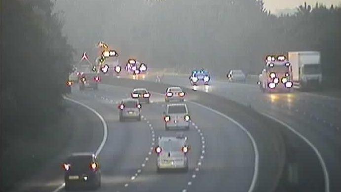 A traffic camera picture, which shows traffic flowing on the eastbound carriageway, while a number of vehicles including a lorry, a car and a number of recovery and emergency vehicles are stopped on the westbound carriageway. 