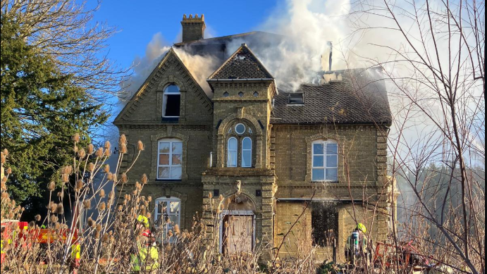 A large Victorian house in yellow/grey brick, with smoke billowing from the roof