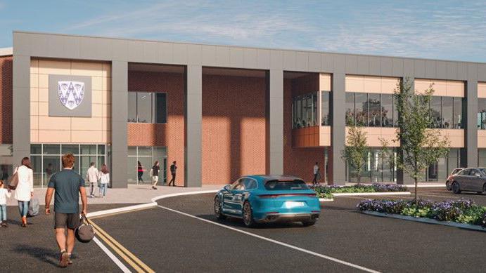 An artist's impression of a sports village. It has a large Shropshire shield on the front, glass windows and a car park. There are people walking towards it and a car driving on a road
