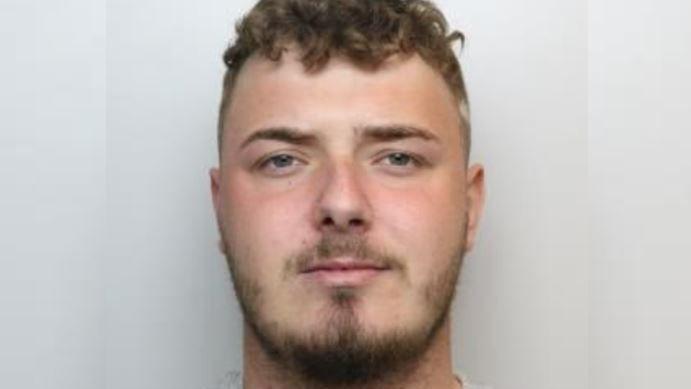 A police custody image of a man with short brown hair and a brown close-trimmed beard.