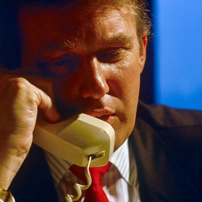 Donald Trump speaking on a cream telephone pictured against a blue background