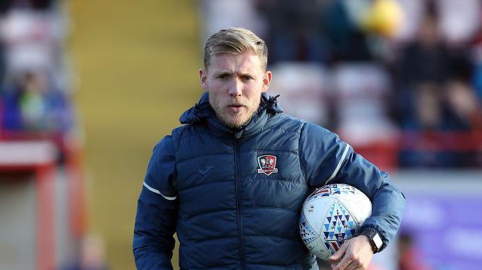 Exeter City coach Dan Green holding a football.