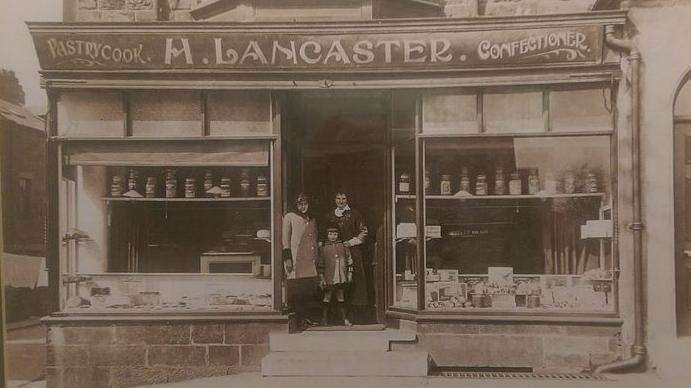 An old photo of a couple and their child standing in the doorway of a bakery.