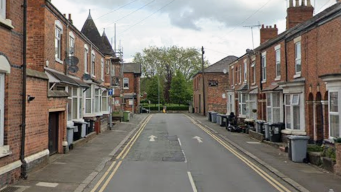 Streetview shot of a street of traditional terraced properties, many with bins outside.