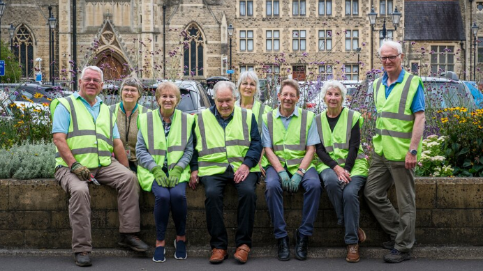 Eight people sit on a low stone wall as they pose for a picture. They're all wearing florescent yellow jackets. 