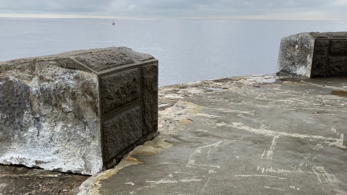 A section of the parapet wall on the edge of North Pier in Tynemouth. A number of blocks are missing and there are scratches in the pavement.