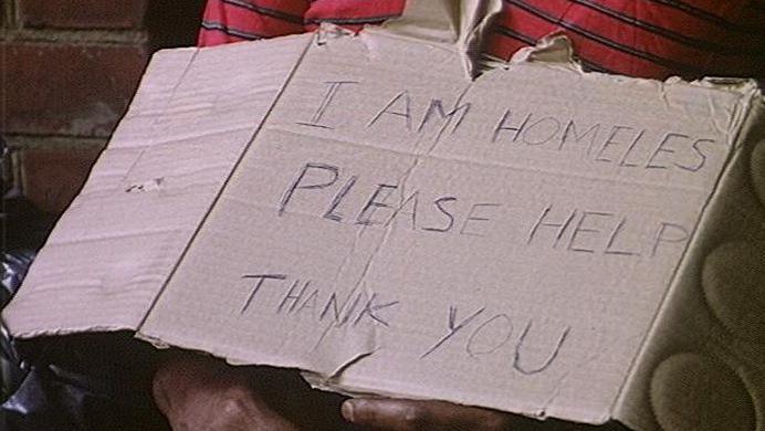 A homeless man holds a sign asking for help