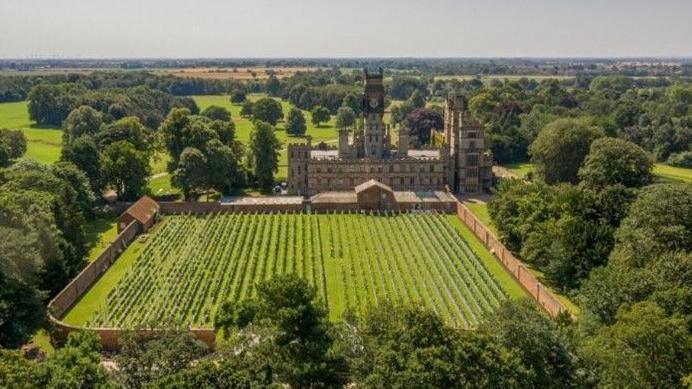 An aerial view of a stately home called Carlton Towers, surrounded by fields and trees, with a walled garden at the front which is planted with vines. 