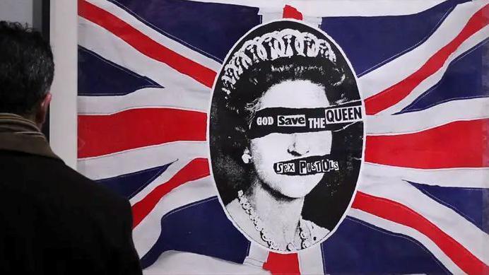 Back of man looking at Sex Pistols artwork featuring a Union Jack and the face of the late Queen.