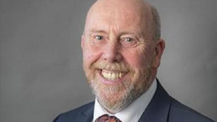 Headshot of Reg Kain looking at the camera and smiling. He is wearing a suit and tie. 