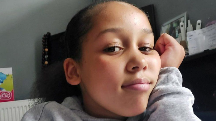 Kyra Hill, smiling at the camera resting her hand on her cheek.