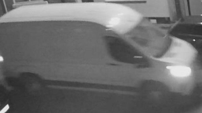 A black and white CCTV image of a white van with its headlights on.