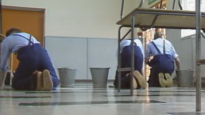 Archive footage of three boys wearing light blue shirts and blue overalls scrubbing the floors by hand at Eastwood Park. 