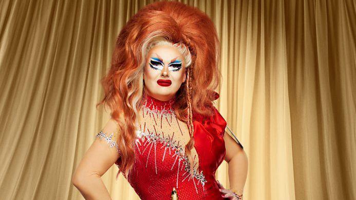 Drag queen Just May in a red wig, colourful make-up and a red dress