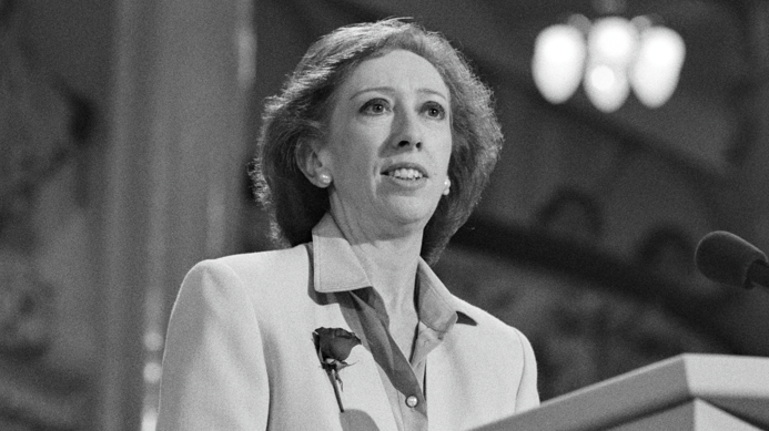 A black and white image of a woman standing at a lectern
