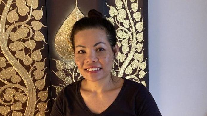 A woman in a black t-shirt with her hair in a bun standing in front of a decorative wall of golden leaves