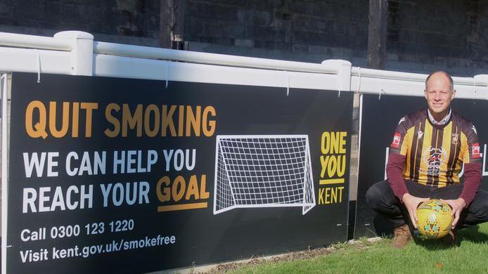 Councillor Dan Watkins teams up with Folkestone Invicta Football Club for the day and checks out KCC’s pitch side banner promoting stop smoking services