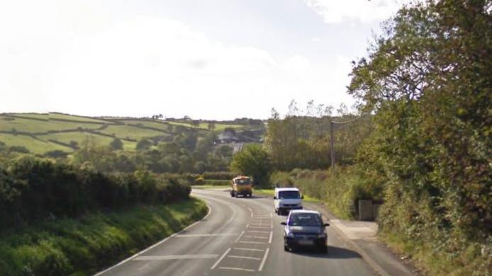 Cars driving along the New Castletown Road with trees either side and hills behind.