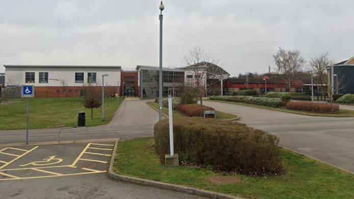 A low-lying school building with a two-storey glazed front and a road leading to the front.