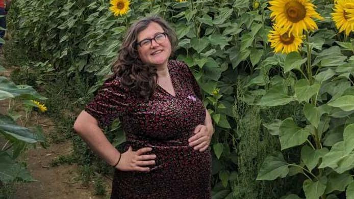 Alice Topping standing in front of a row of sunflowers while pregnant
