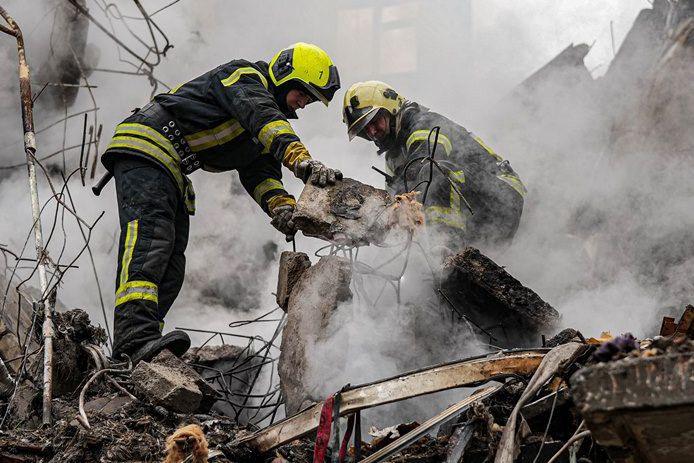 Two firefighters clear rubble in a smoky, dusty scene with broken bits of the building around them, after a strike collapsed a five story residential building in the Sumy region of Ukraine on 13 March 2024.