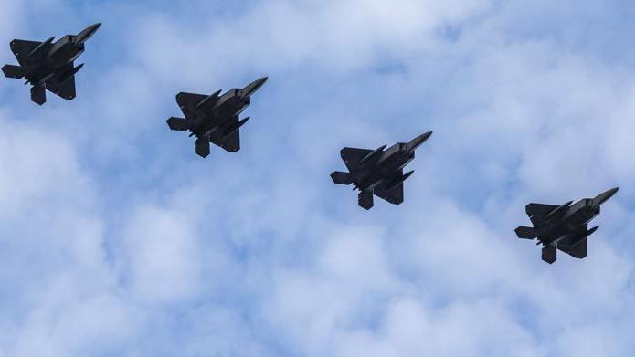 Four fighter jets flying in formation. They are silhouetted against a blue sky with some clouds.