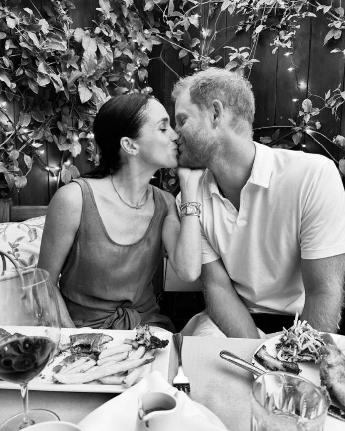 Meghan and Harry kiss each other as they pose against a garden setting in casual wear (her in a dark-coloured singlet, him in a light-coloured short-sleeved polo-style top)  in a black and white Valentine's Day picture.