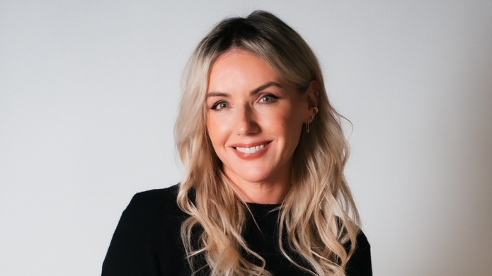 Sali wears a black top and is smiling at the camera. It's a professional headshot.  She has wavy blonde hair.