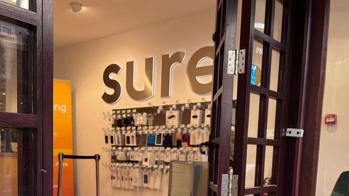 The open door to a mobile phone shop, with phone products hanging on a wall and a Sure sign.