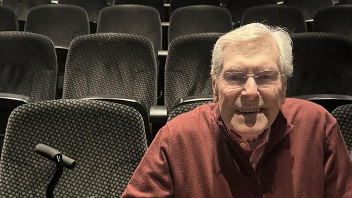 A man smiling sat in the seats of a cinema