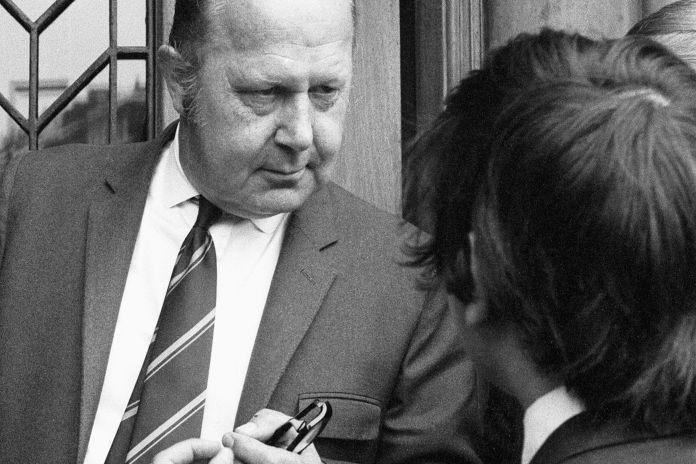 Bank manager at the door of the bank, talking to a man. Both are wearing suits